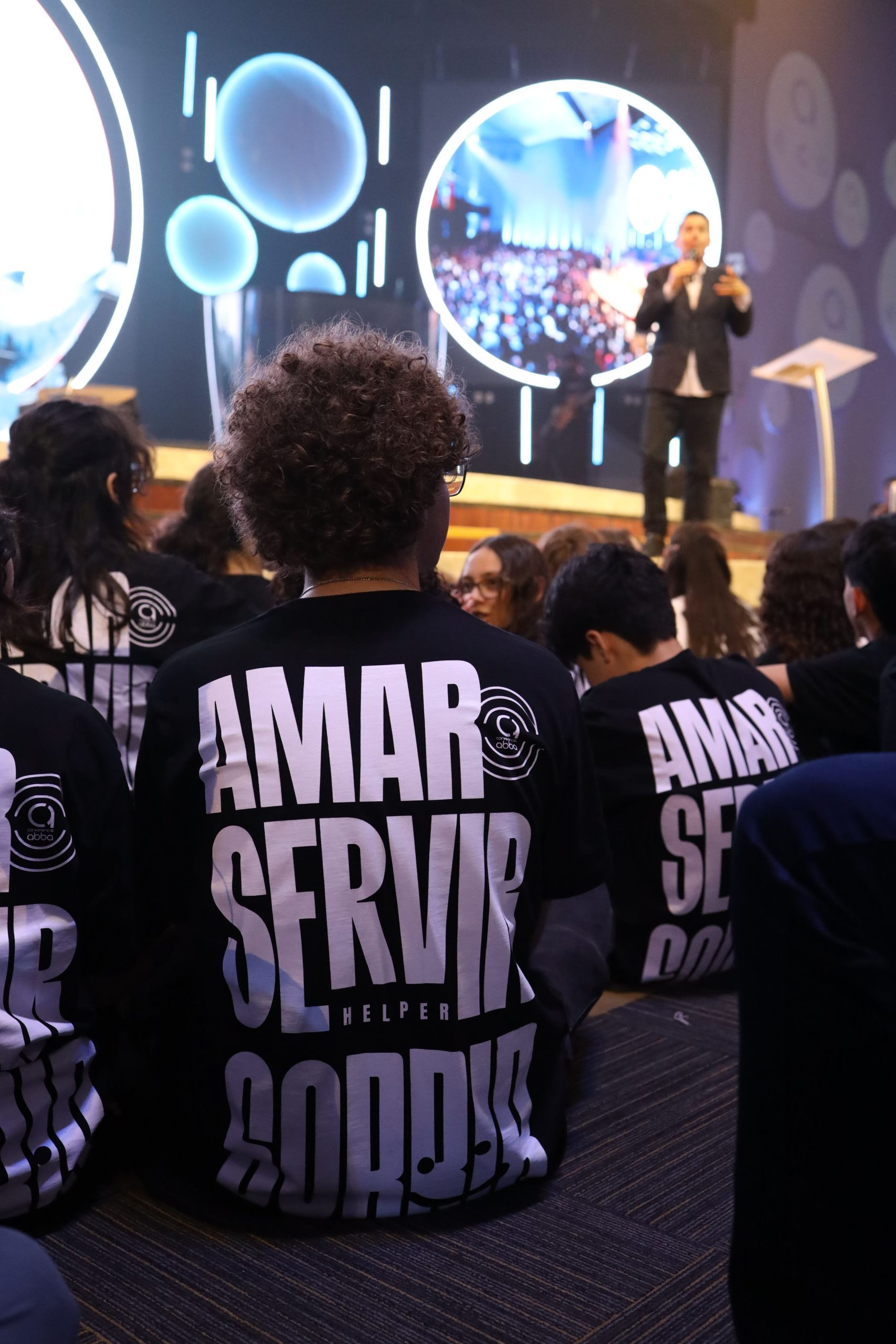 Helpers sentados de frente para o palco, com as camisetas da equipe